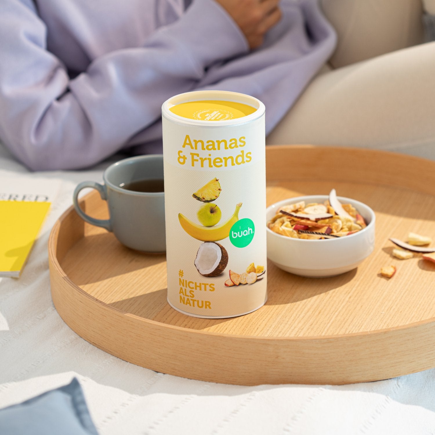 buah Dose Ananas & Friends steht auf Tablett neben Kaffee und einer Schale der Mischung