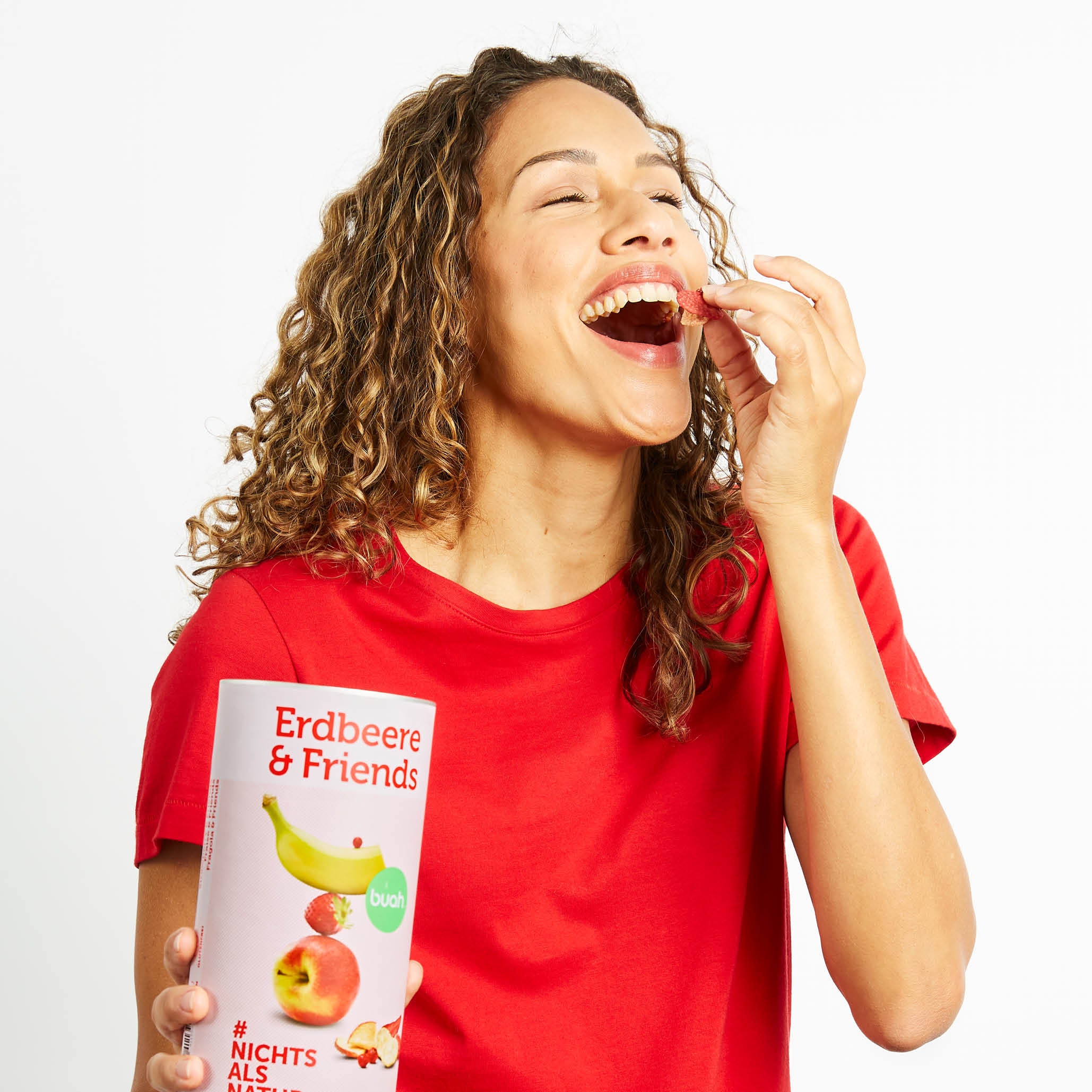 Lachende Frau mit Locke und rotem T-Shirt isst aus einer Dose buah Erdbeere & Friends