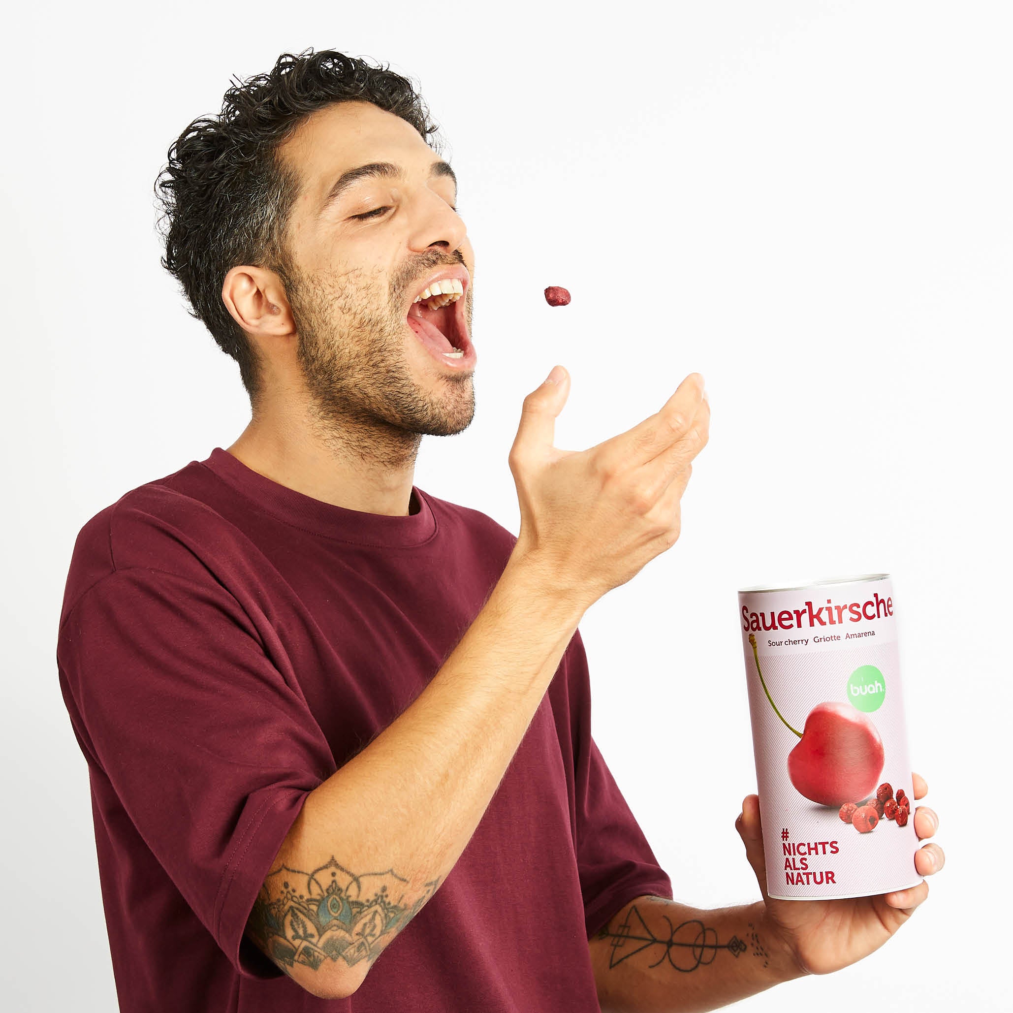 Junger Mann in rotem Shirt wirft sich eine buah Sauerkirsche in den Mund
