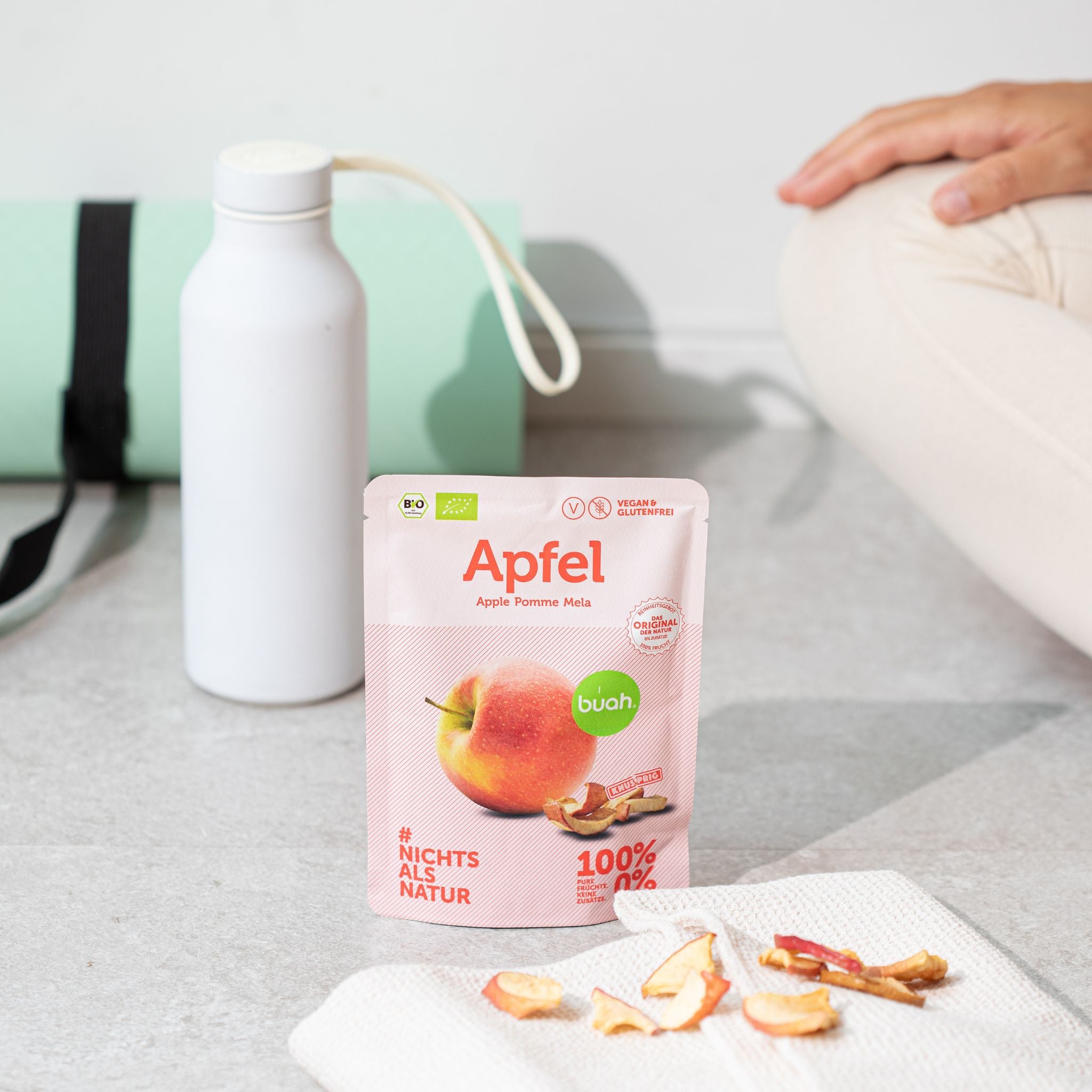 buah Snackpack Apfel in rechteckiger Form steht auf Boden neben Trinkflasche und Sportmatte