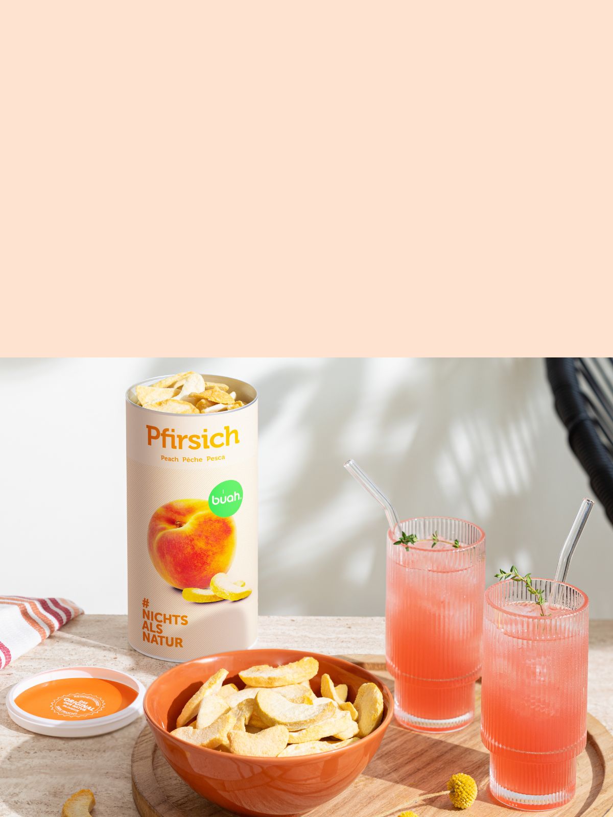 Schale mir buah gefriergetrocknetem Pfirsich auf Holztablett, daneben zwei Pfirsich Mocktail, im Hintergrund buah gefriergetrockneter Pfirsich in grosser Dose