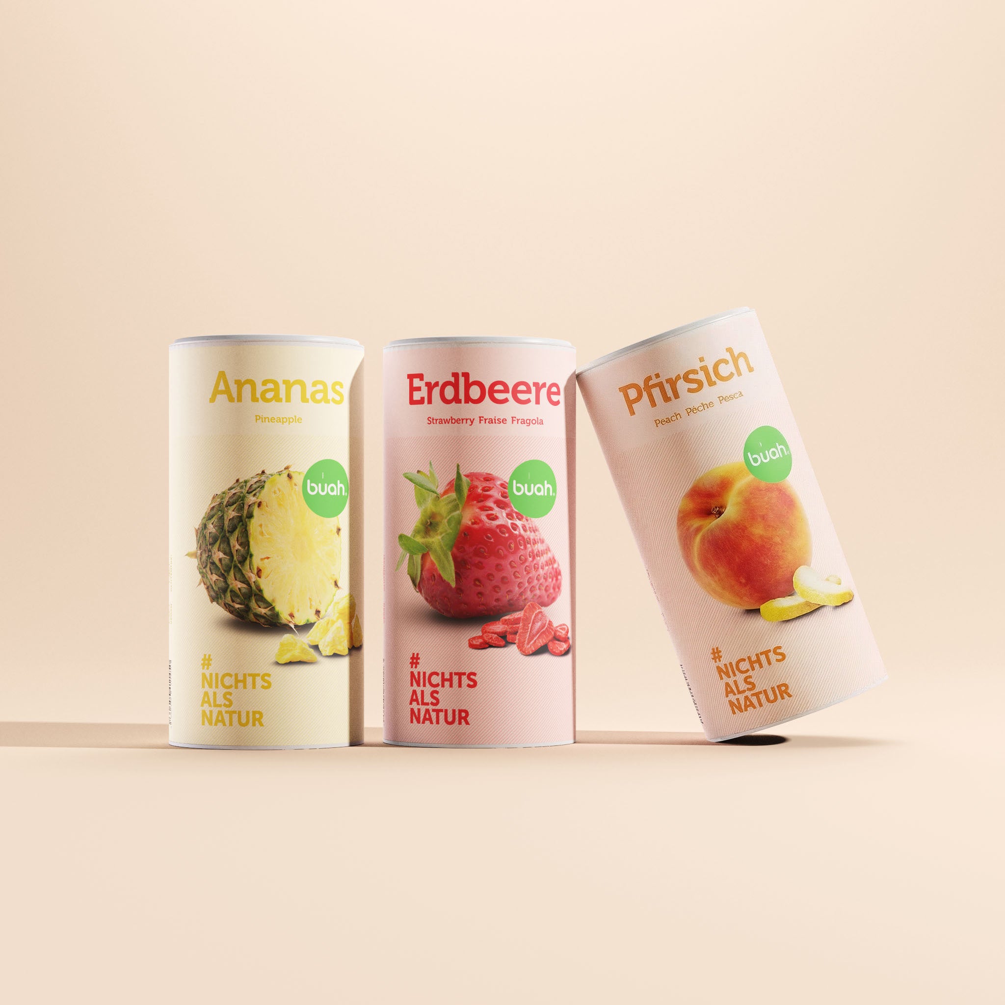 buah Refresh-Set. Drei groĂźe Dosen buah gefriergetrocknete FrĂĽchte in den Sorten Ananas, Erdbeere und Pfirsich stehen vor einem beigefarbenen Hintergrund. Die rechte Dose mit der Sorte Pfirsich ist leicht nach rechts gekippt.