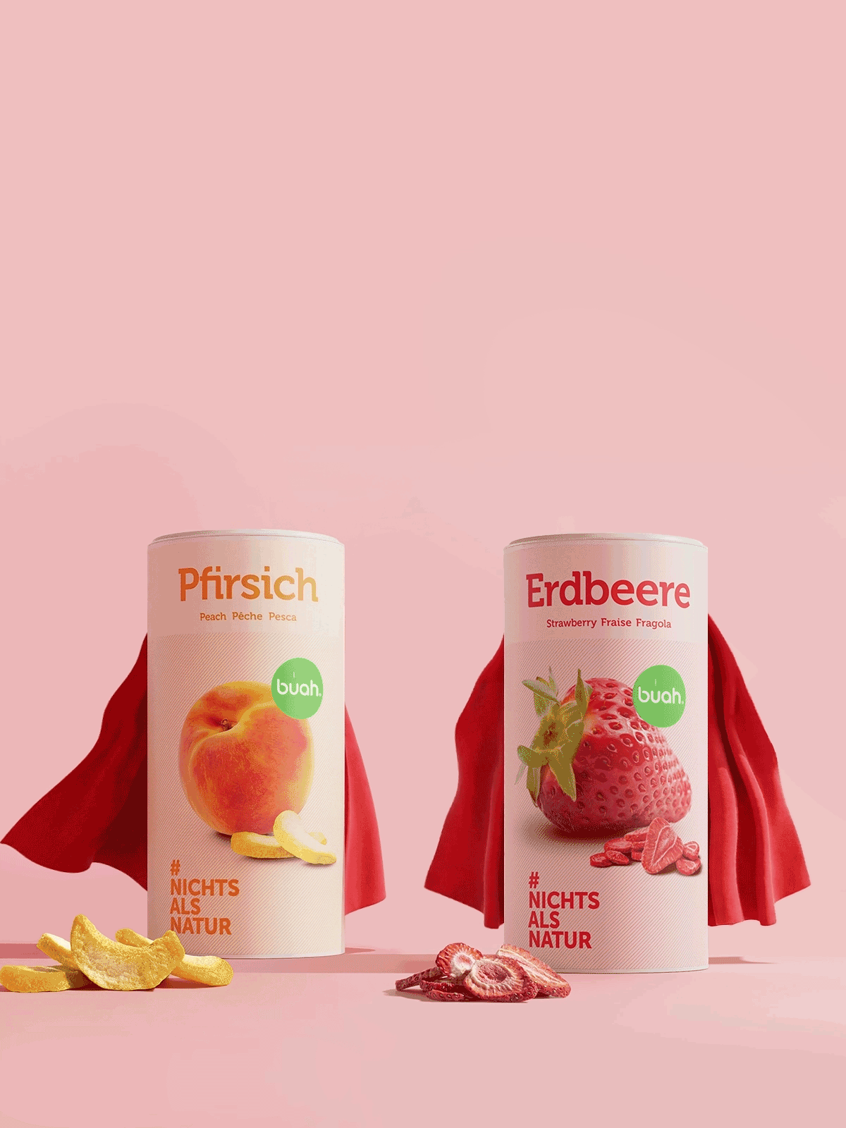 Ein animiertes Bild im Hochformat: Zwei große Dosen buah gefriergetrocknete Früchte der Sorten Pfirsich und Erdbeere stehen auf pinkem Hintergrund. Sie sind mit roten Superhelden-Umhängen ausgestattet, die sich fließend im Wind bewegen. Im Vordergrund liegen Fruchtstücke.