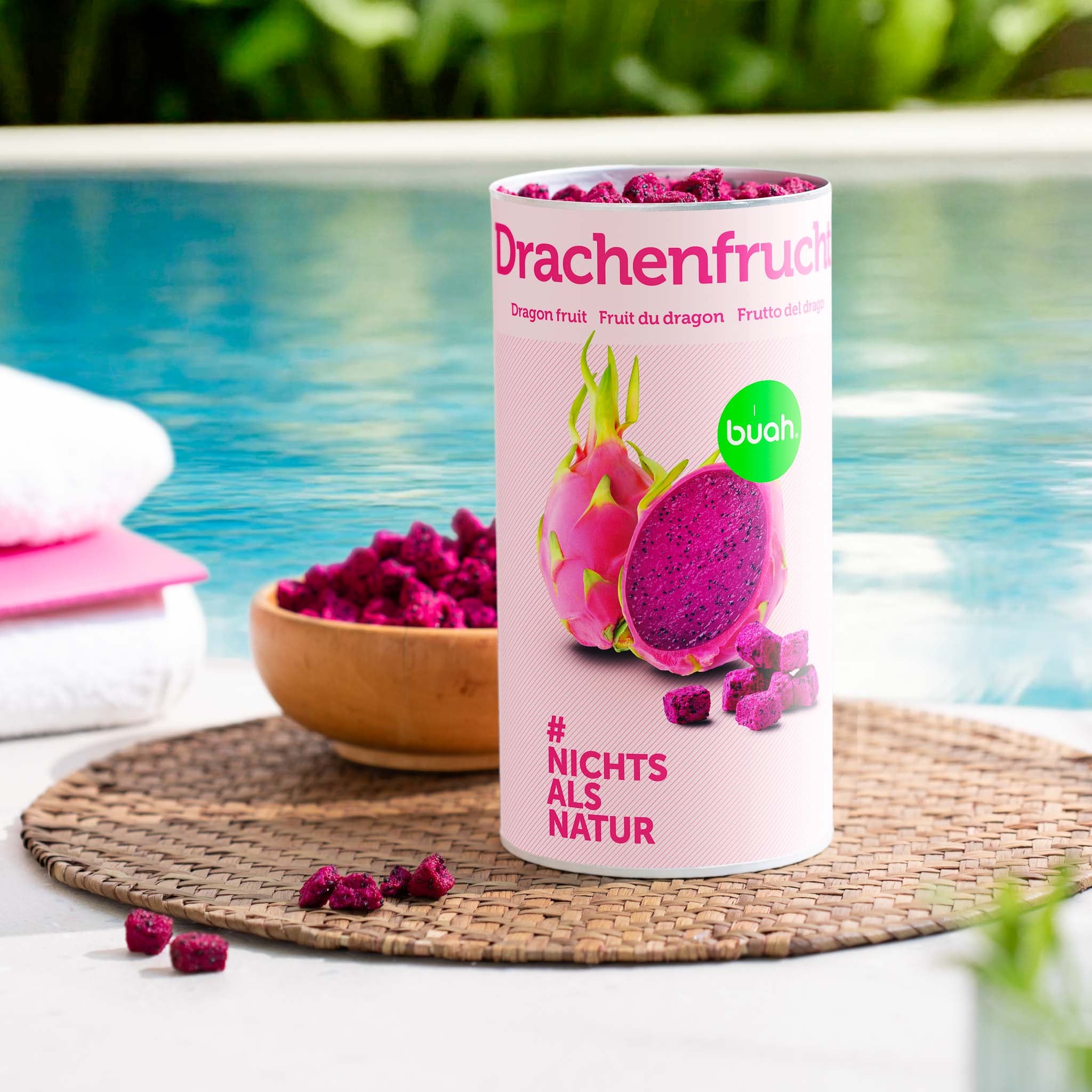 buah gefriergetrocknete Drachenfrucht in er grossen Dose steht neben einem Pool, danaben eine Schale mit pinker Drachenfrucht und Strandhandtuecher