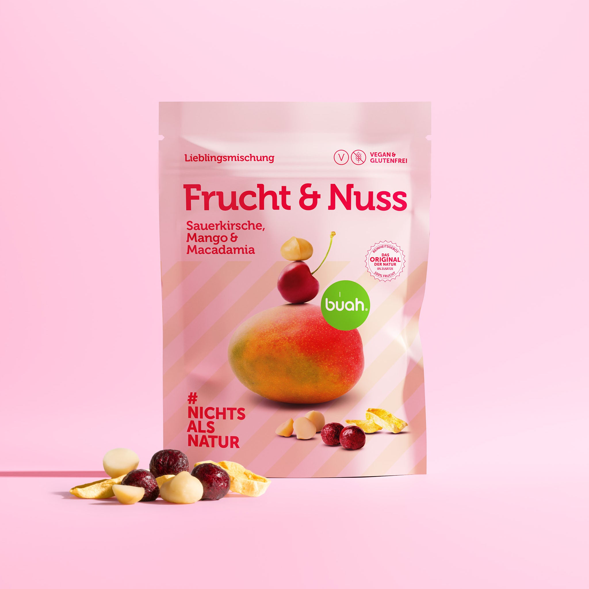Neue buah Frucht & Nuss Mischung mit gefriergetrockneter Sauerkirsche, Mango und Macadamia Nuss vor rosa Hintergrund und Fruchthaufen vor der Packung.
