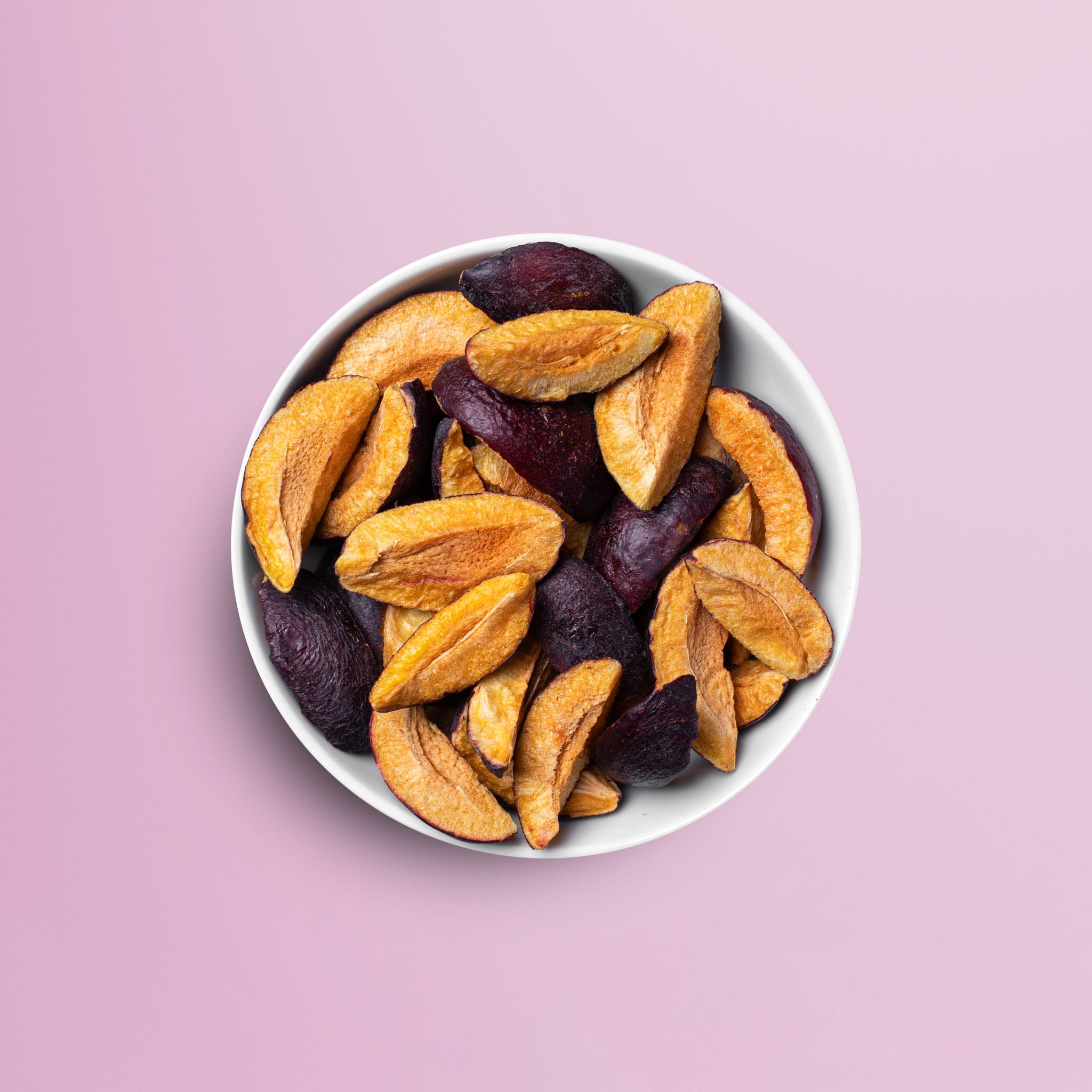 Weisse Schuessel vor rosa Hintergrund mit vielen Schnitzen der buah gefriergetrockneter Pflaume