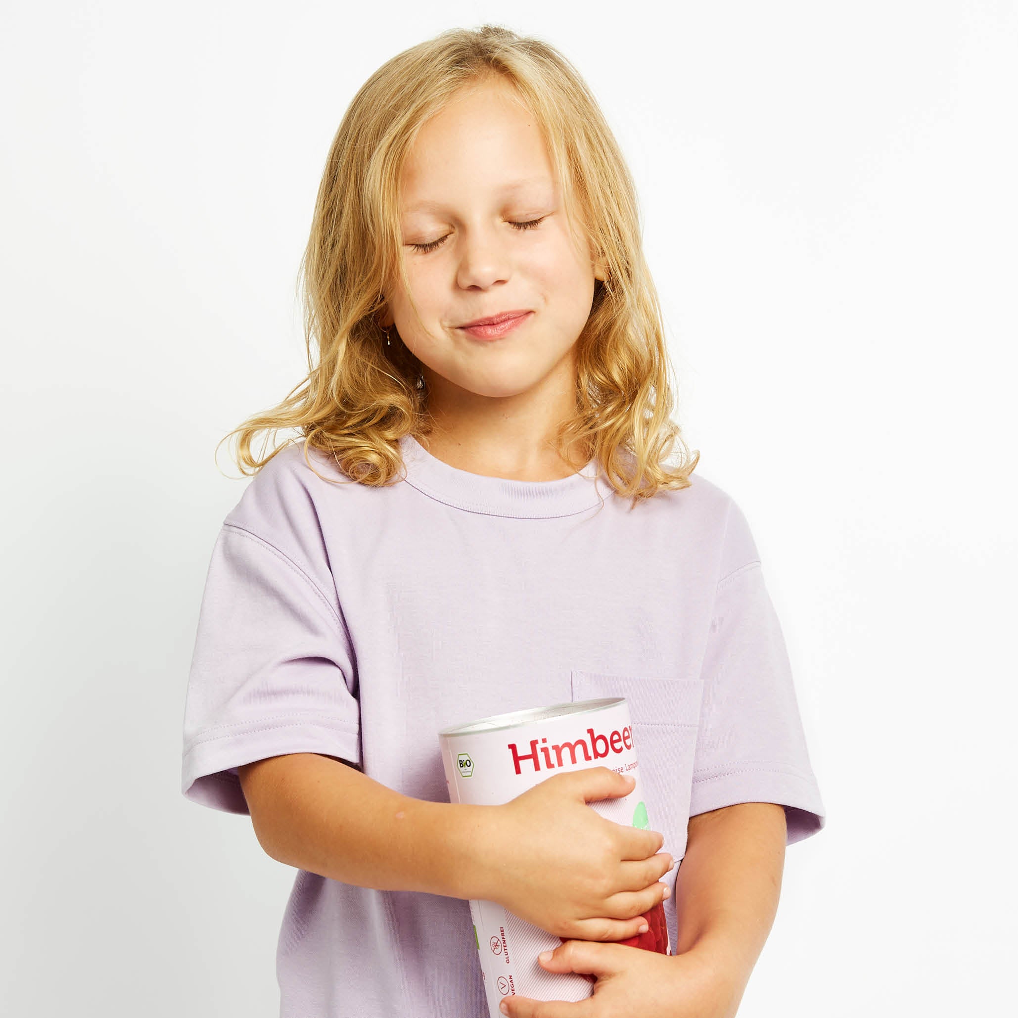 Kind mit geschlossenen Augen und lila Shirt hat eine Dose buah Himbeeren in der Hand