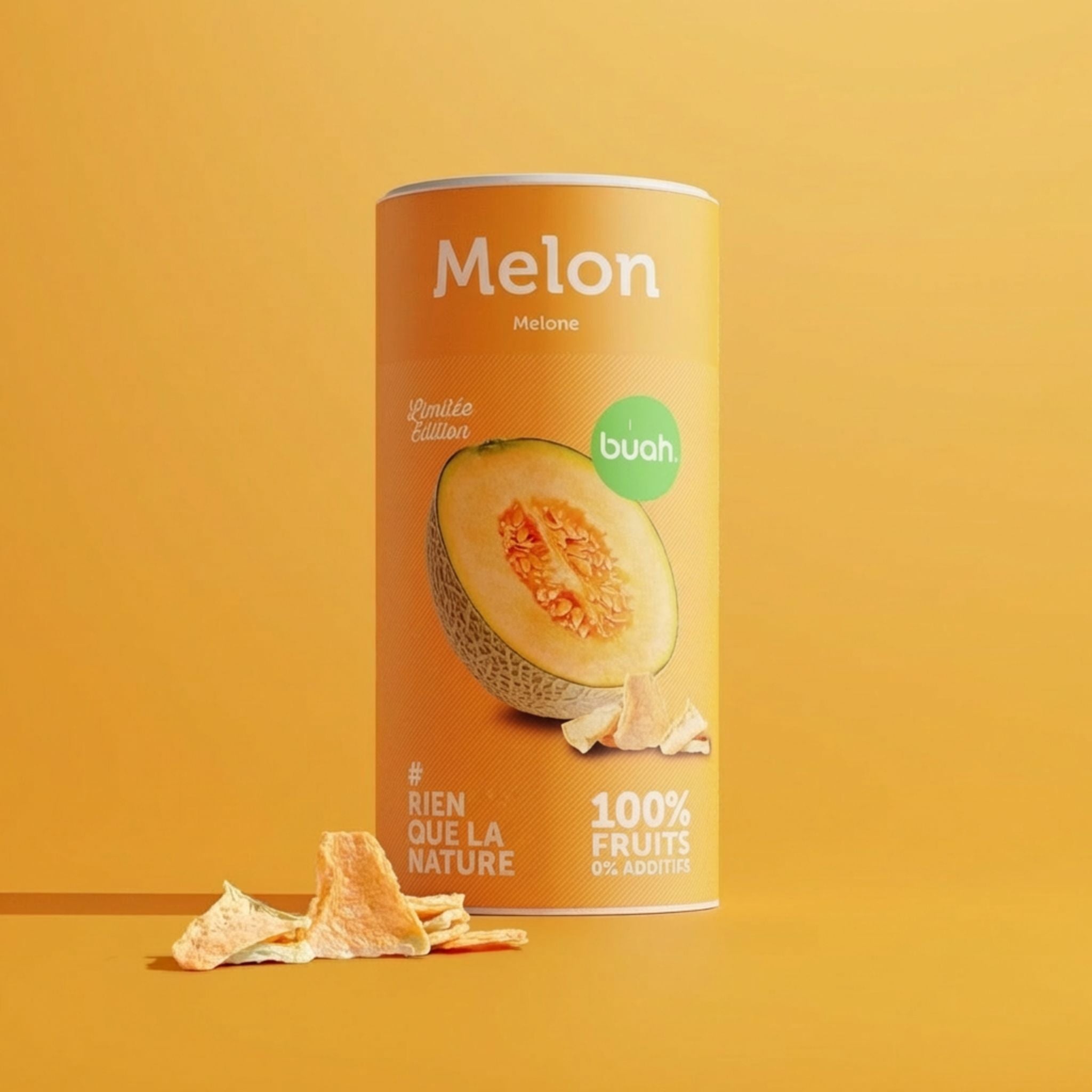 buah Melone. Une boîte orange de fruits lyophilisés buah à la saveur melon (édition limitée) est présentée sur un fond jaune avec quelques morceaux de fruits secs disposés devant la boîte.