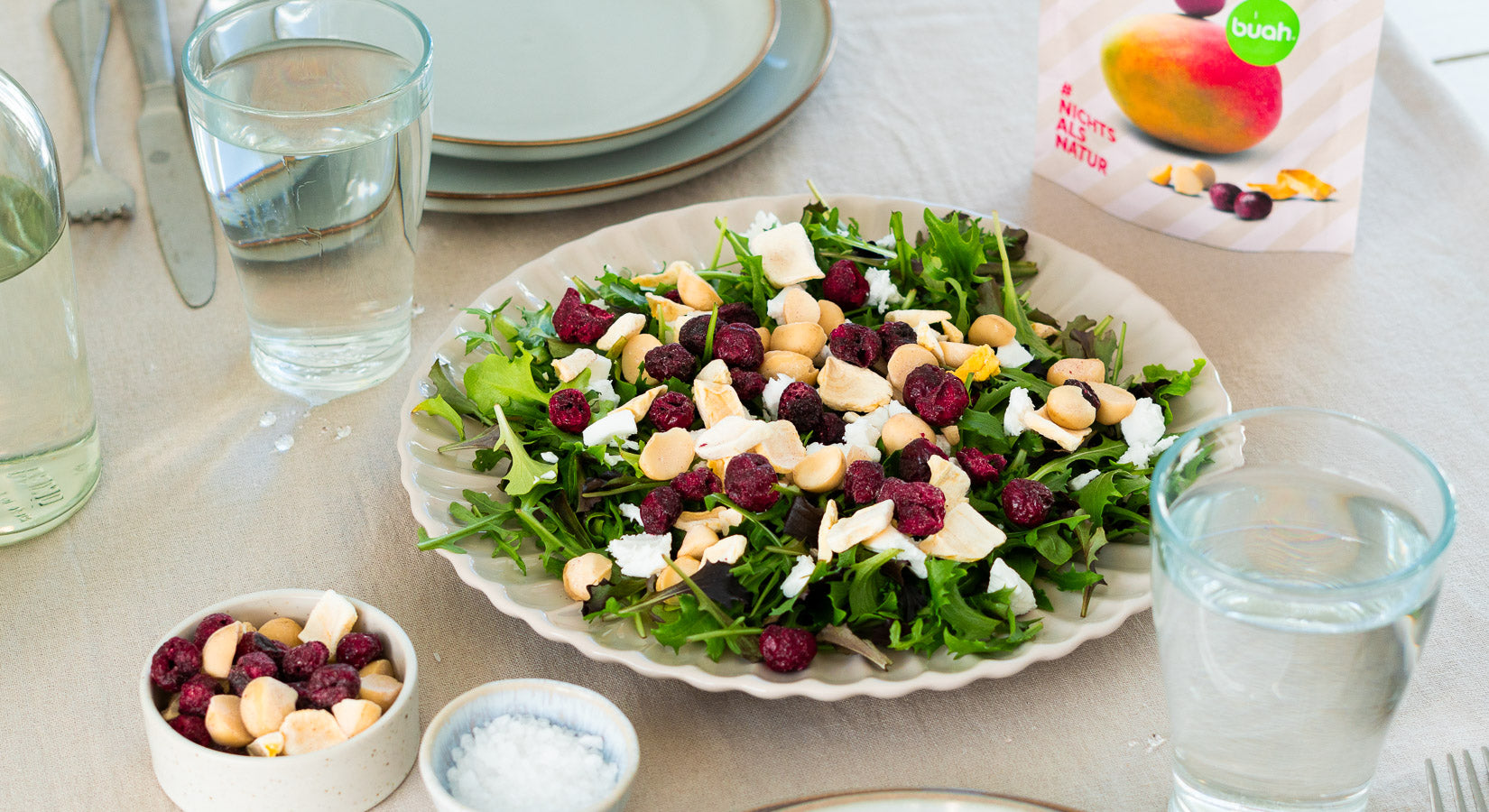 Rucola Salat in einer flachen weißen Schale mit der neuen buah Frucht & Nuss Mischung aus Sauerkirsche, Mango und Macadamia als Topping 