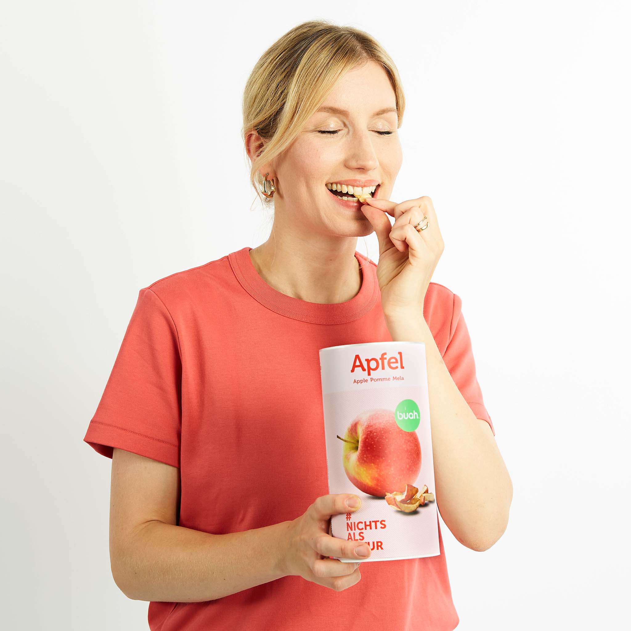 Junge Frau mit blonden Haaren und rosa Shirt snackt buah gefriergetrockneter Apfel aus einer grossen Dosen buah Apfel