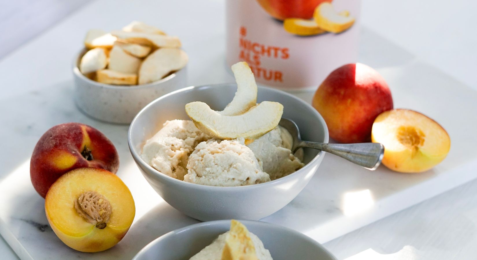 Drei Kugeln Eis in einer Schale mit buah Pfirsich als Topping und frischen Pfirsichen neben dem Eis