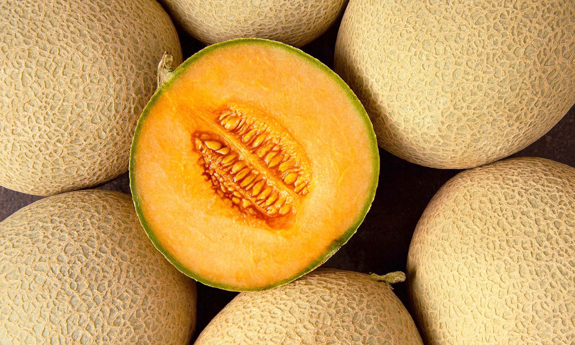 Viele frische Honigmelonen mit saftigem orangenem Fruchtfleisch liegen auf und nebeneinander aufgeschnittene Melone in der Mitte.