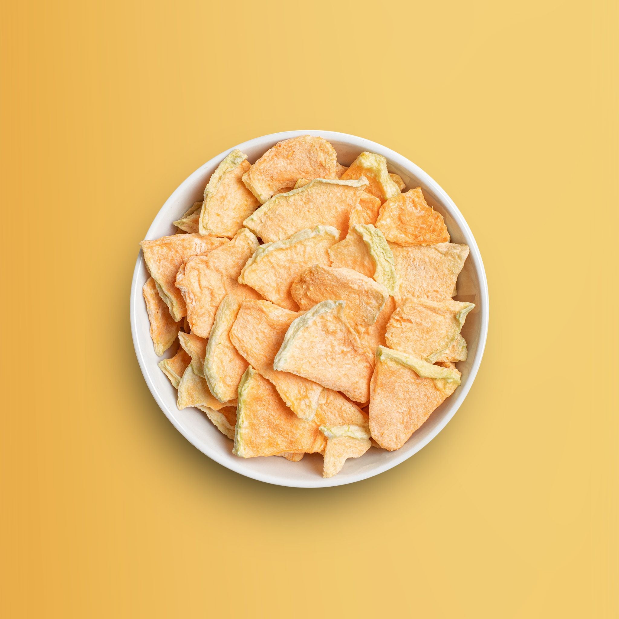 Weisse Schale vor orangenem Hintergrund gefuellt mit buah gefriergetrockneter Cantaloupe Melone in grossen knackigen Stuecken. 