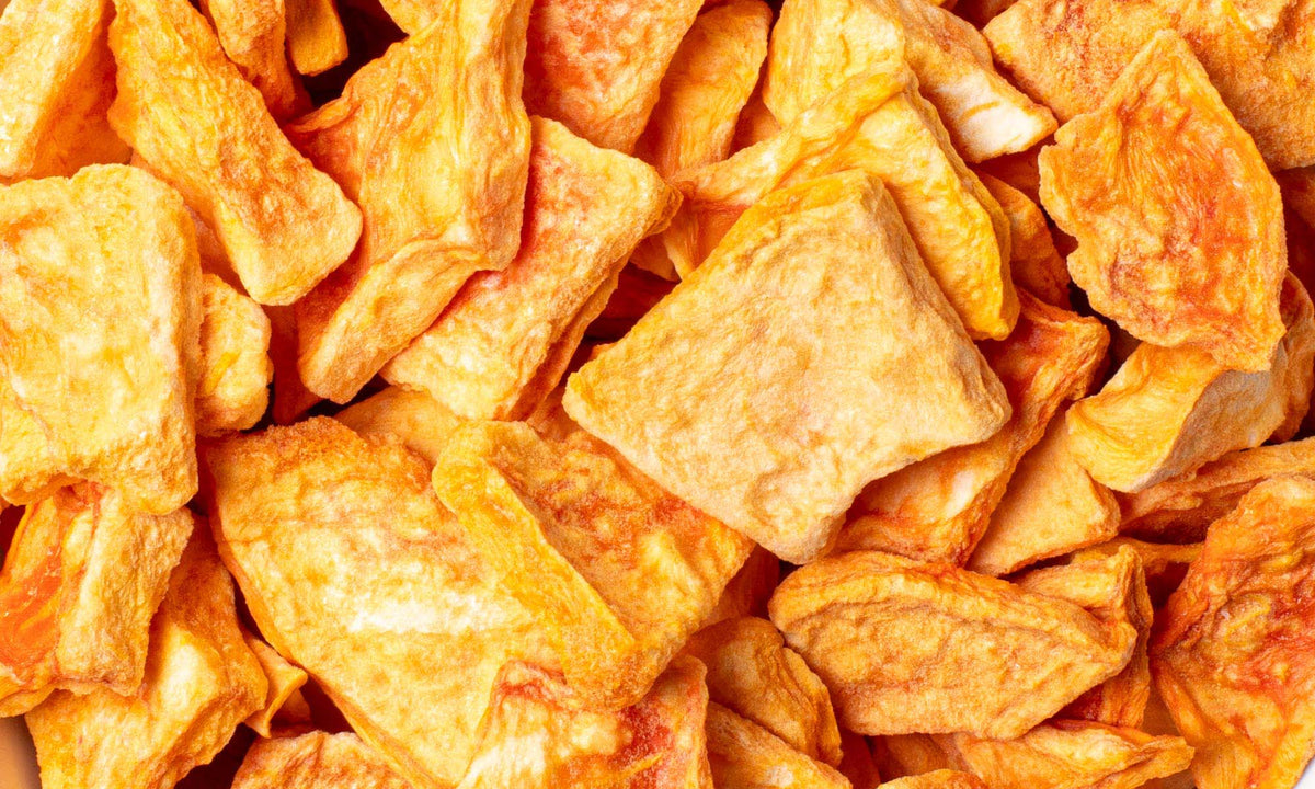 Nahaufnahme unregelmäßiger orangefarbener Stücke gefriergetrockneter Papaya, die die gesamte Bildfläche ausfüllen.